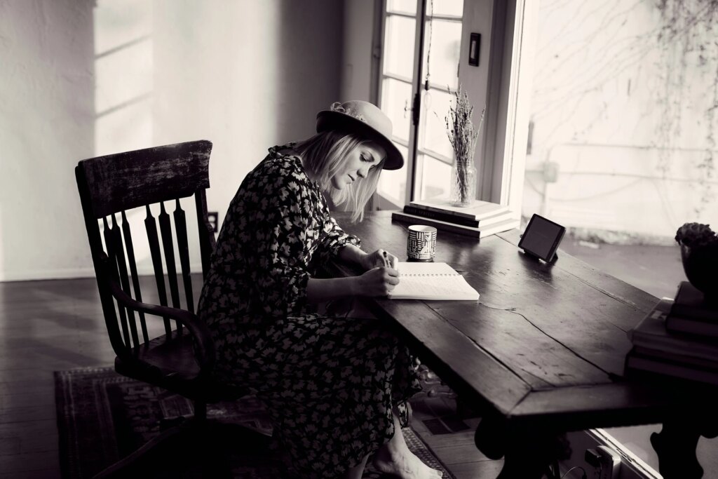 A woman at a table, engaged in writing in a book.