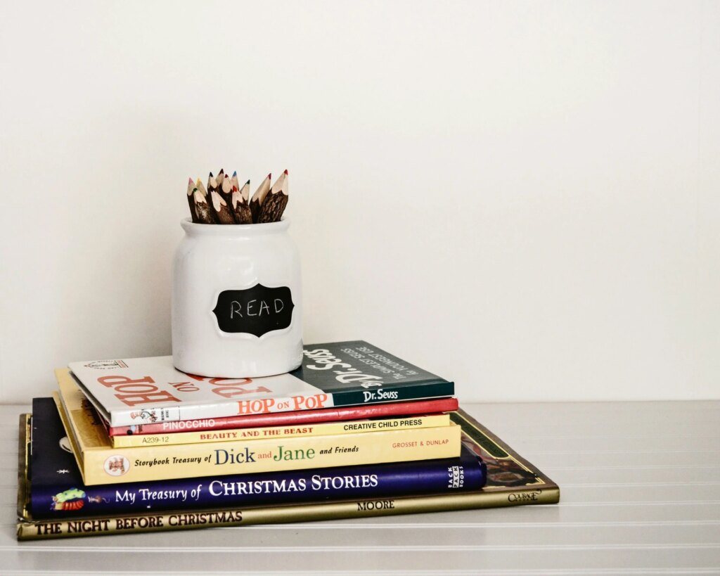 A white jar containing pencils rests on a pile of books.