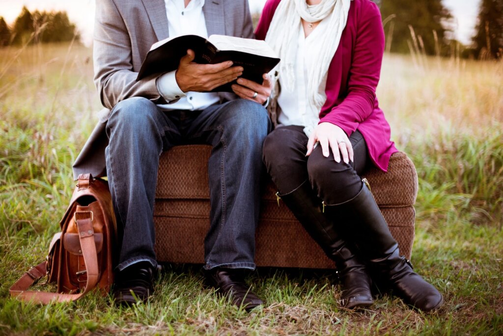 A man reading a book and a woman are sitting on a brown couch.